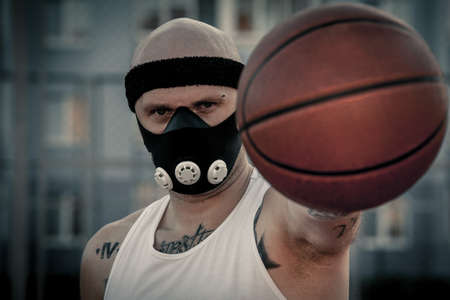 Brutal man in a mask standing on basketball court with Ball in hand and looking at camera.の写真素材