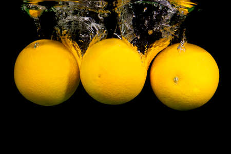 Fruit falling into the water. Flying splashes and drops on a black background. Orange.の写真素材