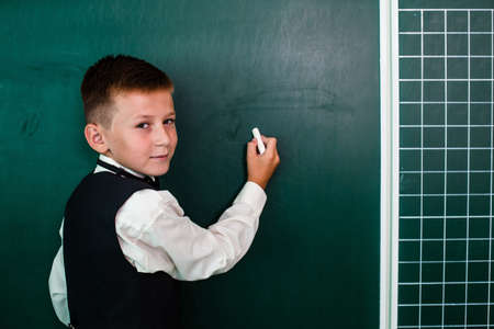 Happy boy writing on the green blackboard with chalkの写真素材