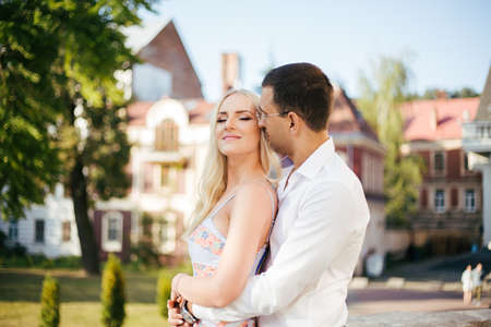 Lovely couple walking around the block. Dark-haired man in a white shirt hugging a blonde in a beautiful dressの写真素材