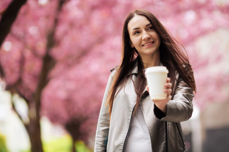 brunette girl in jacket and jeans in the spring outdoors in the city against the backdrop of...