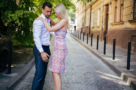 Lovely couple walking around the block. Dark-haired man in a white shirt hugging a blonde in a beautiful dressの写真素材