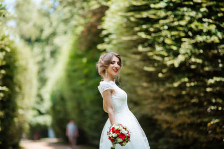 brunette bride in a dress with a wedding bouquet in the park on a background of greeneryの写真素材