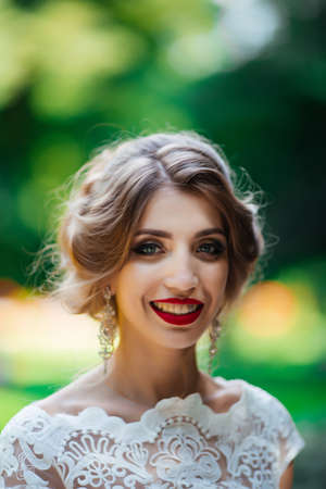 brunette bride in a dress with a wedding bouquet in the park on a background of greeneryの写真素材