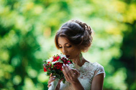brunette bride in a wedding dress and a bouquet at sunset in the parkの写真素材