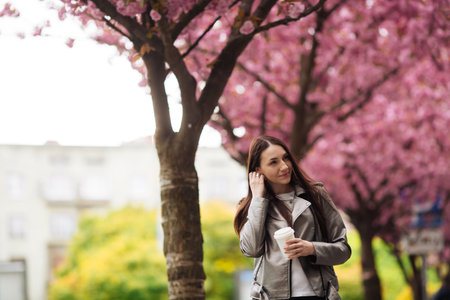 brunette girl in jacket and jeans in the spring outdoors in the city against the backdrop of...