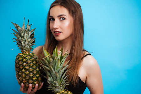 Portrait of young woman in swimsuit with pineapple on blue background. Summer seasonの写真素材