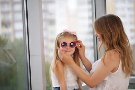 Mother and her baby girl playing hugging against the backdrop of a panoramic windowの写真素材
