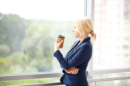 Portrait of a young businesswoman smiling confidently, standing with arms crossed windows in a modern office building overlooking the cityの写真素材