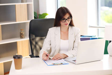 business lady in a light jacket sitting at the table has a laptopの写真素材