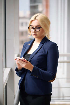 Portrait of a young businesswoman smiling confidently, standing with arms crossed windows in a modern office building overlooking the cityの写真素材