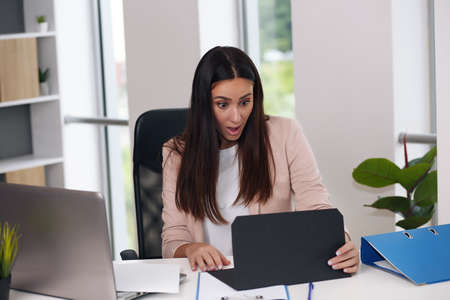 Happy businesswoman with raised so hand gesture reading letter on desk in front of laptop. The businessman is satisfied with the good news from the correspondence.の写真素材