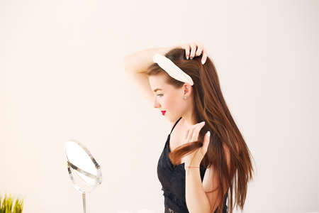 Beautiful girl in home clothes brings beauty to the face in front of a mirror.の写真素材