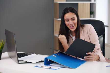 Excited satisfied businesswoman celebrating business success motivated by great financial work result in report, cheerful employee reading letter or notice with good news happy about job promotionの写真素材