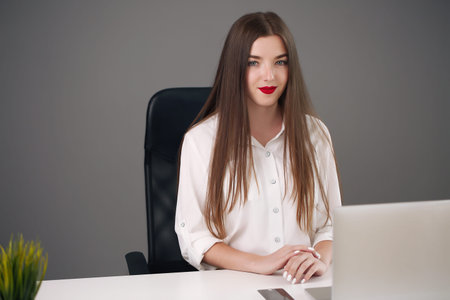 Young woman sitting at a desk with a laptop in a gray office. student or businesswoman