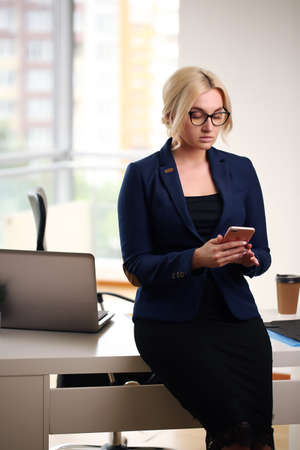 Young blonde businesswoman sitting at desk in the officeの写真素材