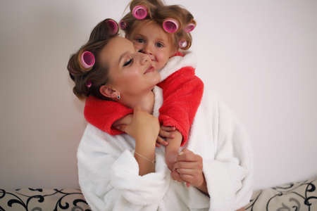 mom and daughter and bathrobe having fun on the couch, having fun in hair curlersの写真素材