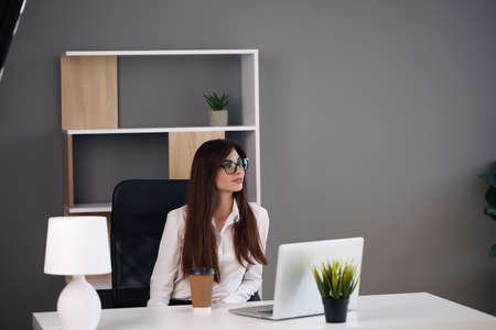 Beautiful business woman uses a laptop and smiles while working in the officeの写真素材