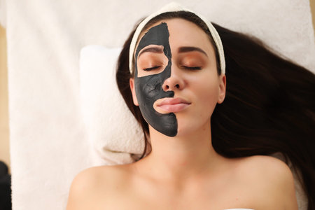 Beautiful woman having clay facial mask apply by beautician.