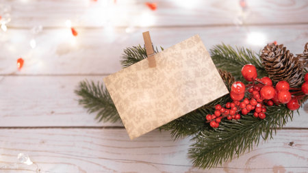 a business card on a clothespin on a fir twig with red berries on a white wooden background , a concept of Christmas and a Christmas greeting card with a place for text and advertisingの写真素材