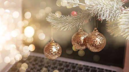 three golden Christmas tree balls on a fir branch on the background of a laptop and a bokeh , the concept of Christmas 2022の写真素材