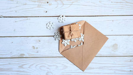 an open craft envelope lies on a white wooden background and small white snowflakes pour out of it with a place for the text , the concept of Christmasの写真素材
