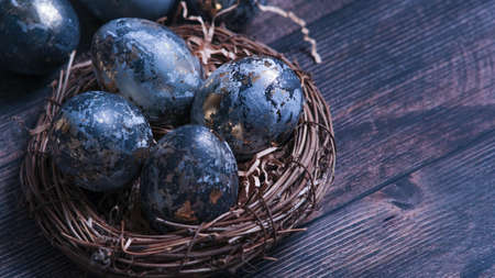 Easter card with a copy of the place for the text. Very Peri 2022 .Purple, blue eggs in a basket on a dark newspaper background. Natural dye karkade tea.の写真素材