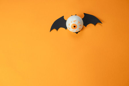 white toy eye with wings of a flying mouse on an orange background , Halloween concept