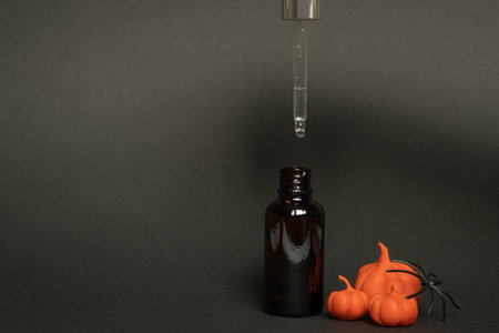 a black serum bottle on a black background with plasticine pumpkins and a spider , a creative Halloween conceptの写真素材