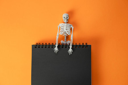 black notebook on a spring with a toy skeleton on an orange background , a creative Halloween...