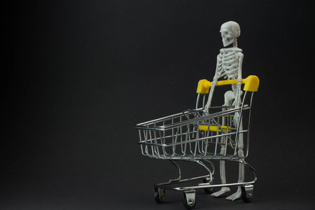 a skeleton carries an empty cart from a supermarket on a black background, the concept of shopping...