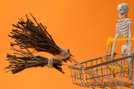 a skeleton is driving a supermarket cart with a witchs broom on an orange background, the concept of shopping sales in honor of the Halloween holidayの写真素材