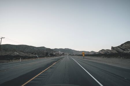 Empty Highway in California Right after Sunset with Yellow Road Sign and Mountains in the distance during Coronavirus Pandemicの写真素材