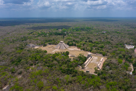 Aerial view of the beautiful Chicen Itza and Mayan Pyramid in Mexico surrounded with ground and greenery with ocean under cloudy sky during dayの写真素材