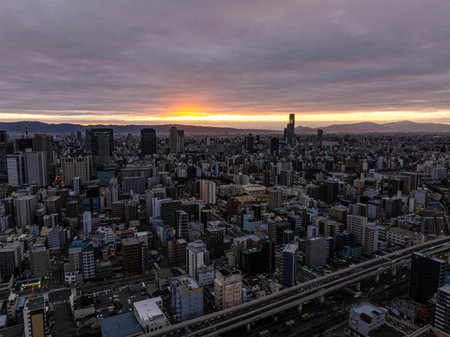 Beautiful golden hour sunrise over Osaka's urban skyline, with mountains in the distance and a highway running through the cityscapeの写真素材