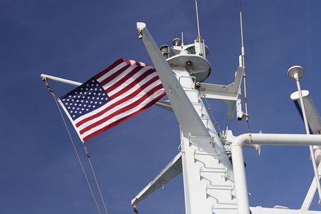 Us Flag on top of a ferry boat flying against the blue sky with a hint of clouds.の写真素材