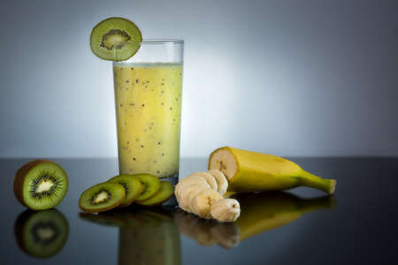 Fresh and juicy banana and kiwi smoothie in glass with fruits around - High quality healthy concept on black and gray backgroundの写真素材