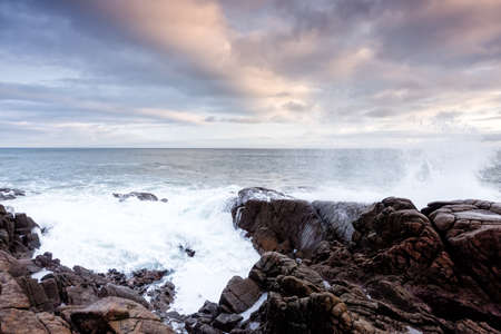 Waves crashes over rocks at the sunrises over the ocean in Northern Irelandの写真素材