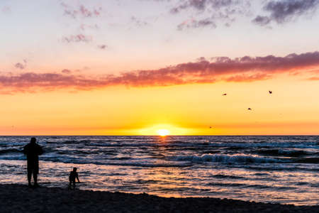 Silhouette of a man and child playing at the beach with beautiful sunset over seaの写真素材
