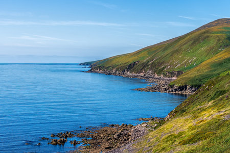 Blue sky and sea with rocky costal line and green hills