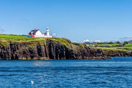 Red and white lighthouse on cliff with village in a distance â view from seaの写真素材