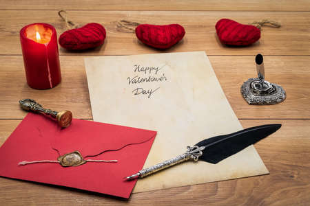 Lovely classic Valentineâs Day cad, hand written with ink and quill on vintage paper, red envelope with wax seal, lit candle, cuddle heart, silver quill stand on oak â front viewの写真素材