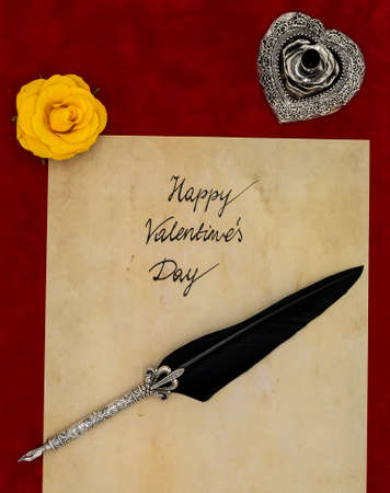 Antique preachment with hand written Happy Valentineâs Day, yellow rose, detailed silver quill stand in shape of hart accented by flat lying beautifully ornamented silver and black quillの写真素材