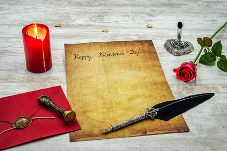 Lovely classic Valentineâs Day cad, hand written with ink and quill on vintage paper, red envelope with wax seal, red rose, lit candle, silver quill stand decorations on white painted oak - front viewの写真素材