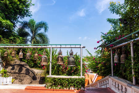 Several Buddha bells hanging in a row surrounded by green trees and flowers, Buddhism concept, Thailandの写真素材