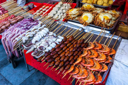 Roasted, fried and raw insects, silkworms, scorpions, bugs, snakes, dog meat, octopus on stick as snack street food in Chinaの写真素材
