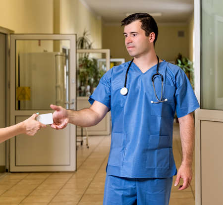 Middle age, Caucasian white, male doctor in scrubs with stethoscope accepting White Card, blurred hospital corridor in backgroundの写真素材