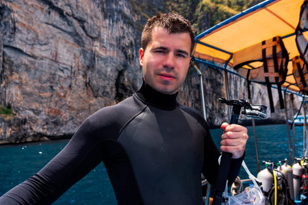 Young Caucasian male scuba diver holding action camera and preparing for diving from boat full of...