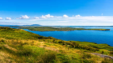 Small village, green fields and meadows on the coast, beautiful coastline and islands, moody blue sky with clouds, Wiled Atlantic Way, Irelandの写真素材