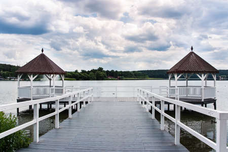Beautiful white roofed pier with wooden huts on lake, green forest and puffy clouds in background, Barlinek, Polandの写真素材